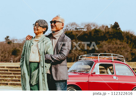 愛車バックに寄り添うシニア夫婦の写真 112322616