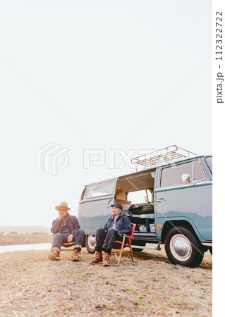 夕暮れの中にアウトドアの椅子に座って佇むシニア夫婦 112322722