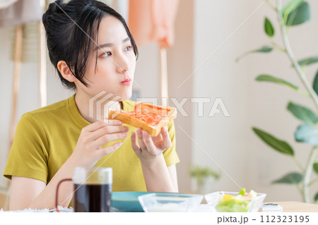 リビングで朝食を食べる若い女性 112323195