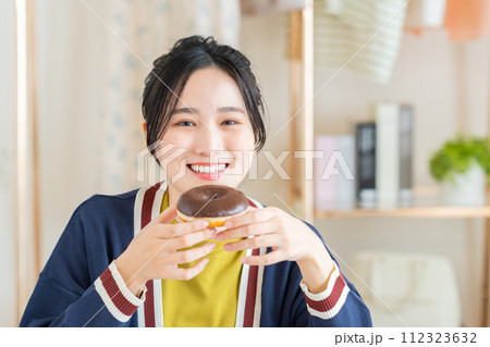 リビングでドーナツを食べる若い女性 112323632