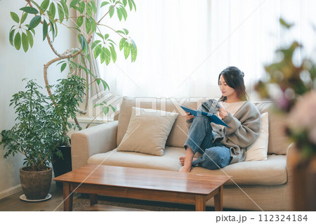 緑溢れるインテリアに囲まれてソファーに座りながら読書する女性 112324184