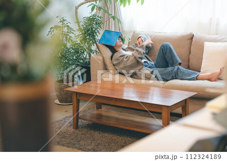 緑溢れるインテリアに囲まれてソファーに座りながら読書する女性 112324189
