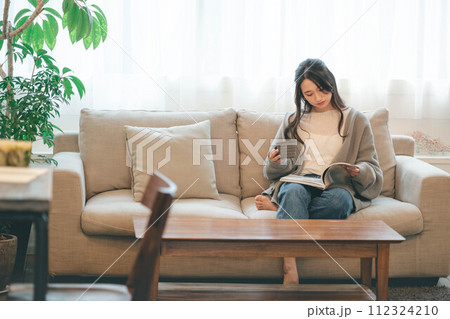 緑溢れるインテリアに囲まれてソファーに座りながら読書する女性 112324210