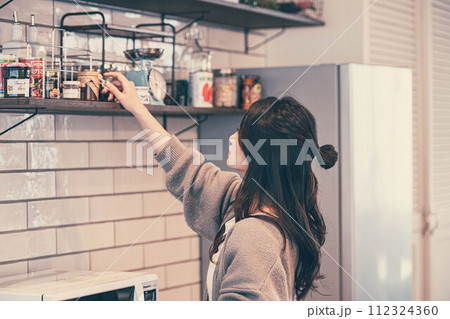 キッチンで調味料を選ぶロングヘアーの女性 キッチンで調味料を選ぶロングヘアーの女性 112324360