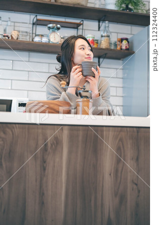キッチンでコーヒーを飲みながら休憩する女性 112324400