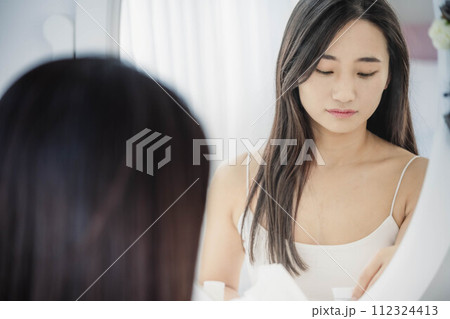 鏡を見ながらスキンケアする若い女性 鏡を見ながらスキンケアする若い女性 112324413