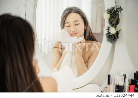 鏡を見ながらスキンケアする若い女性 112324444