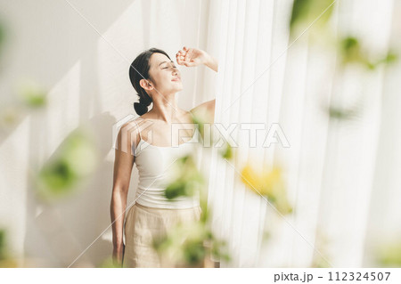 朝に自然溢れる窓際で光を浴びる女性 112324507