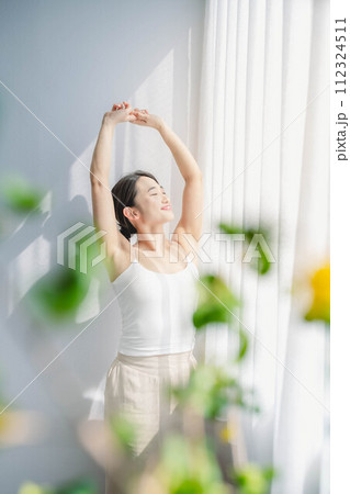 朝に窓際で伸びをする女性 112324511