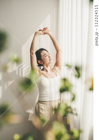 朝に窓際で伸びをする女性 112324515