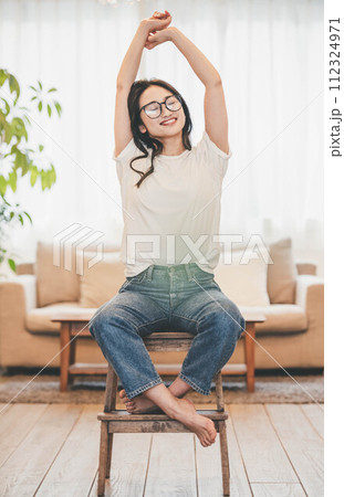 カジュアルな服装で椅子に座っているロングヘアのメガネ女性 カジュアルな服装で椅子に座っているロングヘアのメガネ女性 112324971