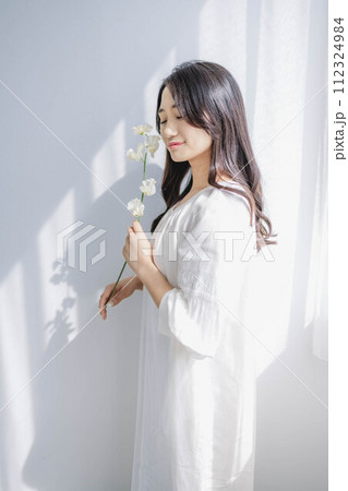 窓際に立ち花を持つ女性 112324984