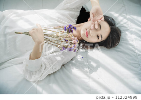 花を持ちベットに寝転ぶ女性 花を持ちベットに寝転ぶ女性 112324999