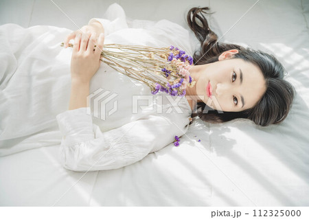 花を持ちベットに寝転ぶ女性 112325000