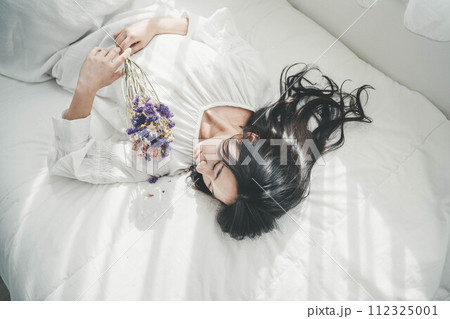 花を持ちベットに寝転ぶ女性 花を持ちベットに寝転ぶ女性 112325001
