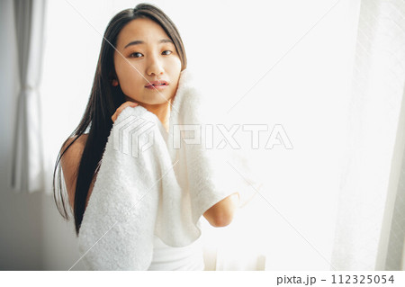 窓際でタオルで顔を拭いている女性 112325054