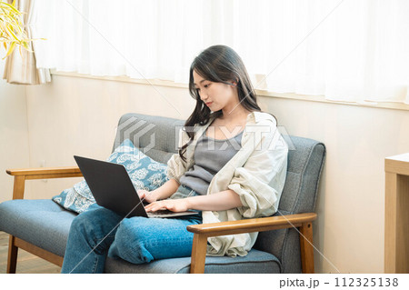 ソファーに座りながらパソコンを操作する女性 112325138
