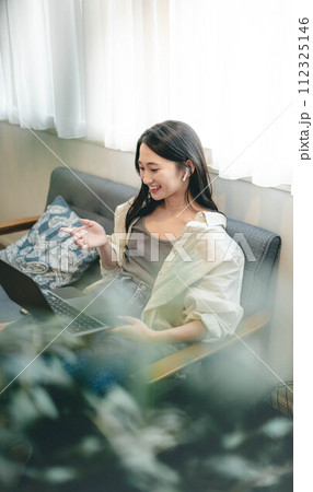 ソファーに座りながらパソコンを操作する女性 112325146