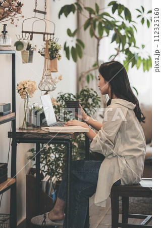 部屋でパソコンと本を広げ仕事する女性 部屋でパソコンと本を広げ仕事する女性 112325160