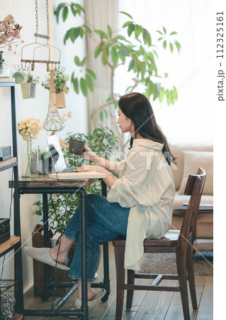 部屋でパソコンと本を広げ仕事する女性 112325161