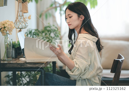 部屋でパソコンと本を広げ仕事する女性 112325162