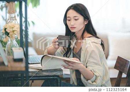 部屋でパソコンと本を広げ仕事する女性 112325164