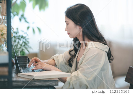 部屋でパソコンと本を広げ仕事する女性 112325165