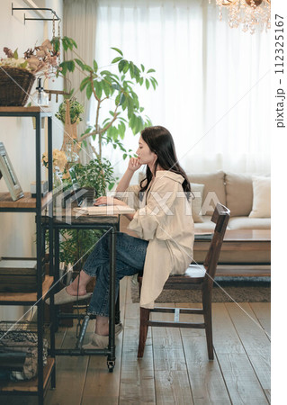 部屋でパソコンと本を広げ仕事する女性 部屋でパソコンと本を広げ仕事する女性 112325167