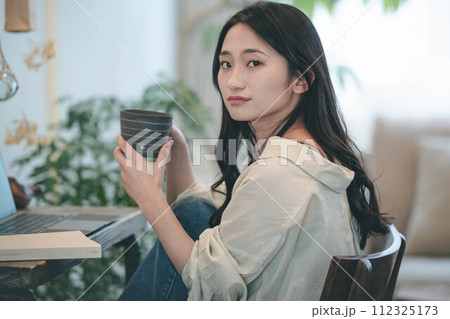 部屋でパソコンと本を広げ仕事する女性 部屋でパソコンと本を広げ仕事する女性 112325173