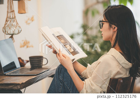 部屋でパソコンと本を広げ仕事する女性 112325176