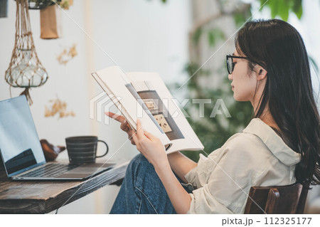 部屋でパソコンと本を広げ仕事する女性 112325177