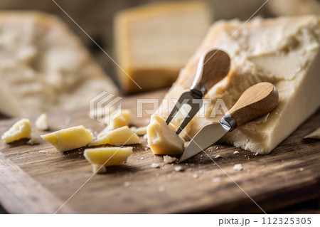 A block and pieces of Parmesan cheese on a cutting board along with a chisel and a skewer A block and pieces of Parmesan cheese on a cutting board along with a chisel and a skewer 112325305