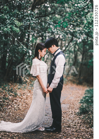 森林の中で向き合う新郎新婦 112330726