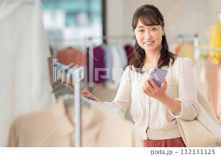 お店でショッピングしながらスマホを操作するミドルの女性 お店でショッピングしながらスマホを操作するミドルの女性 112331125