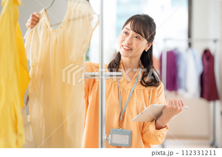 アパレルショップでタブレットを操作しながら働くミドルの女性の店員 112331211