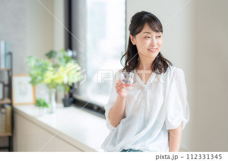 リビングで水を飲むミドルの女性 112331345