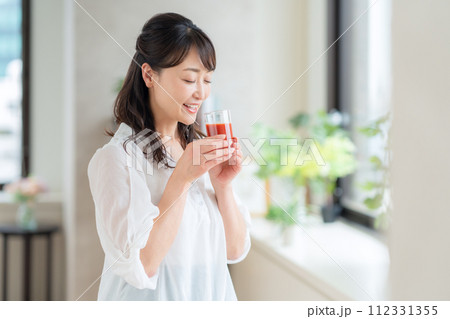 リビングでトマトジュースを飲むミドルの女性 112331355