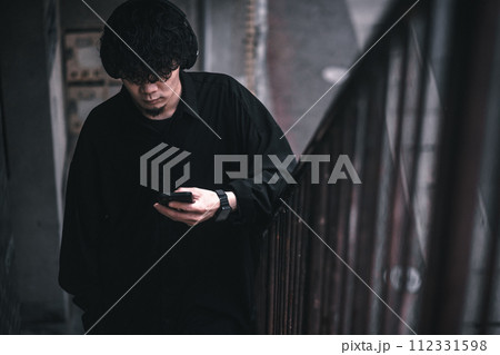 古びたビルの階段でスマホで音楽を聴く男性 112331598