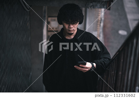 古びたビルの階段でスマホで音楽を聴く男性 112331602