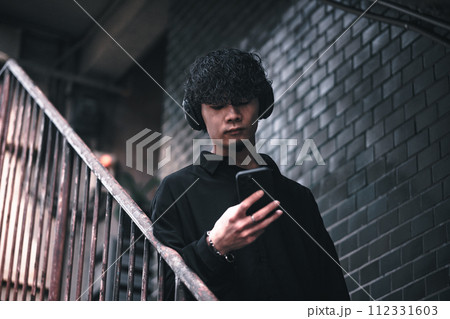 古びたビルの階段でスマホで音楽を聴く男性 古びたビルの階段でスマホで音楽を聴く男性 112331603