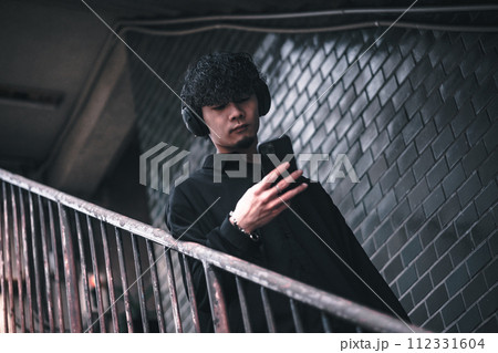 古びたビルの階段でスマホで音楽を聴く男性 古びたビルの階段でスマホで音楽を聴く男性 112331604