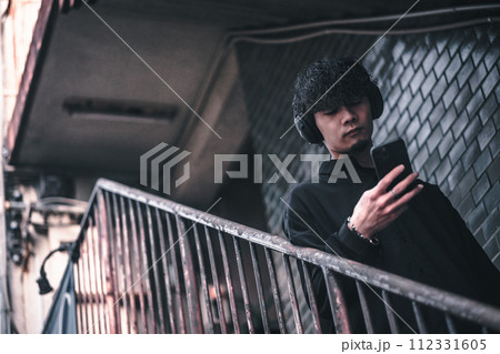 古びたビルの階段でスマホで音楽を聴く男性 古びたビルの階段でスマホで音楽を聴く男性 112331605
