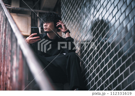 古びたビルの階段でスマホで音楽を聴く男性 古びたビルの階段でスマホで音楽を聴く男性 112331619