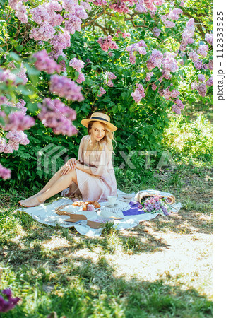 Serene Moment Under Lavender Lilac Blooms in Springtime. woman relaxes with a cup under blooming lilac bushes, enjoying a peaceful spring day. 112333525