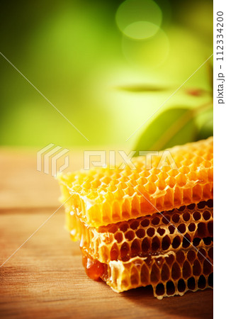 A stack of pure, raw honeycomb on a rustic wooden background, illuminated by natural light. 112334200