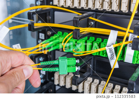 Hand of computer technician connecting fiber optics cable into data switch 112335583