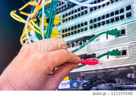 Hand of computer technician connecting network cable into data switch 112335590