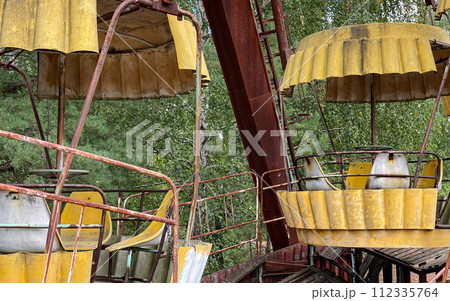 Eerie scene of an abandoned amusement park: a rusting merry-go-round overtaken by nature 112335764