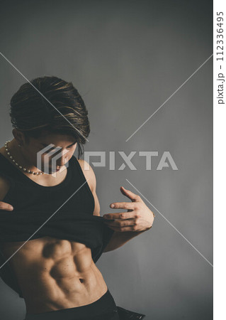 タンクトップを捲り上げて腹筋を見せる若い男性 112336495