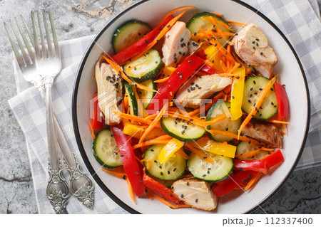 Healthy food Chicken salad with fresh cucumbers, bell peppers, carrots and sesame seeds close-up in a bowl. Horizontal top view 112337400
